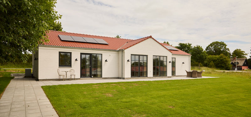 Hvid facade i palæstil fra eurodan-huse med rødt tegltag, sorte sprossevinduer, solceller, fliseterrasse og grøn græsplæne – inspiration til klassisk nybyggeri og husdrømme.