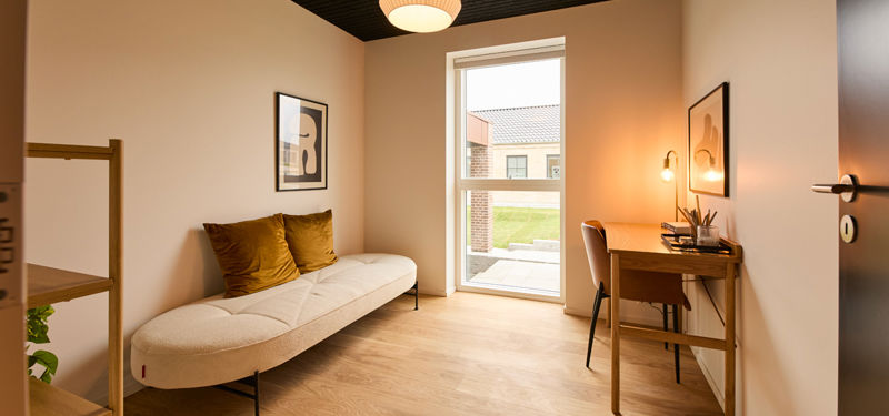 Fleksibelt kontor og gæsteværelse fra eurodan-huse med lys daybed, træskrivebord, væglampe, højt vindue, sort loft og varme puder – inspiration til hjemmekontor i nybyggeri, funktionelt husbyggeri og nye husdrømme.
