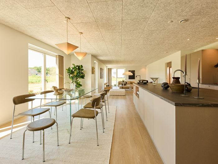 Køkken-alrum fra eurodan-huse med lang køkkenø, mørk bordplade, glasbord, pendellamper, store vinduer og kig gennem huset mod stuen – inspiration til åbent nybyggeri og moderne husdrømme.