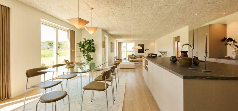Køkken-alrum fra eurodan-huse med lang køkkenø, mørk bordplade, glasbord, pendellamper, store vinduer og kig gennem huset mod stuen – inspiration til åbent nybyggeri og moderne husdrømme.