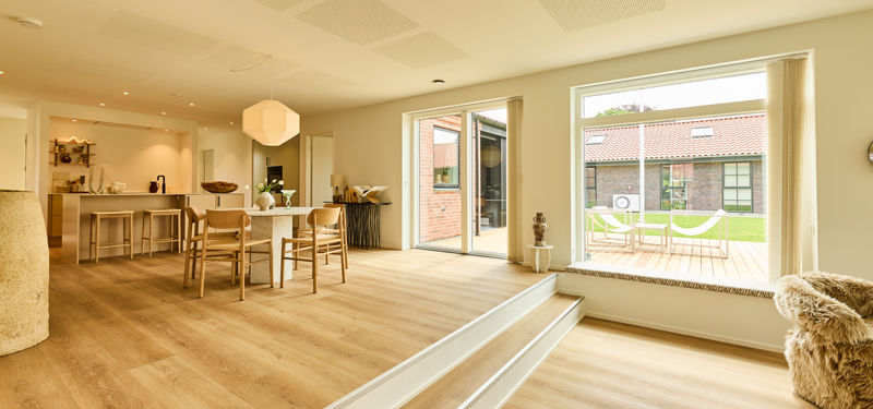 Åbent køkken-alrum og stue fra eurodan-huse med bred indvendig trappe, spiseplads, køkkenø, sansevindue og store glasdøre mod terrasse – inspiration til nybyggeri.