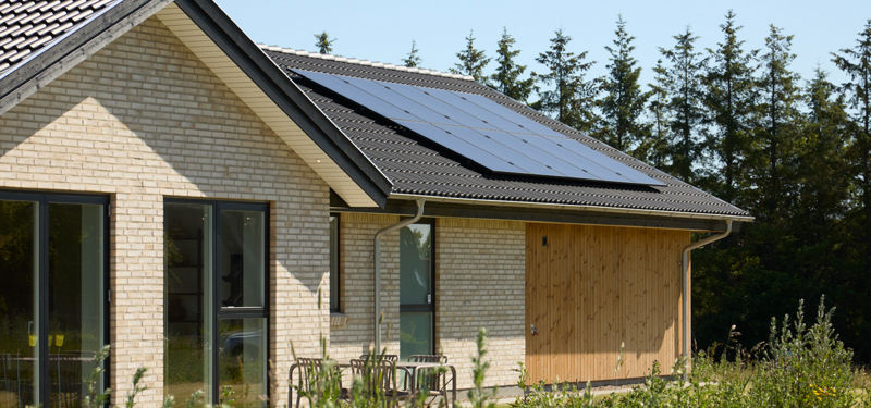 Udefra kig på hus fra eurodan-huse med lyse mursten, sort tag, solceller, træbeklædt carport og sorte vinduer – inspiration til energieffektivt nybyggeri og praktiske husdrømme.