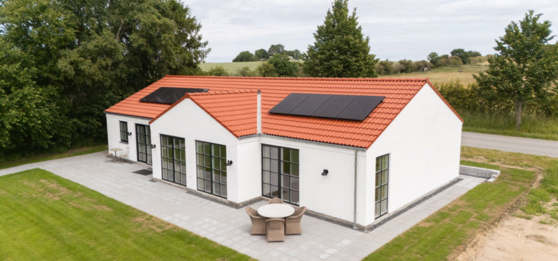 Dronefoto af eurodan-huse udstillingshus i palæstil med hvid facade, rødt tegltag, solceller, sorte sprossede vinduer, terrasse og grøn have – inspiration til klassisk nybyggeri.