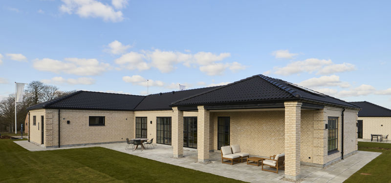 Terrasse fra eurodan-huse ved lys murstensfacade med sort tegltag, store vinduespartier, overdækket uderum og direkte adgang fra boligen til udearealet – inspiration til nybyggeri med praktisk terrasse, husbyggeri og moderne husdrømme.
