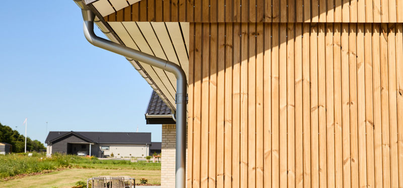Detalje af hus fra eurodan-huse med lodret træfacade, tagudhæng, stern, tagrende og nedløbsrør – inspiration til materialevalg, facadedesign, nybyggeri og moderne husdrømme.