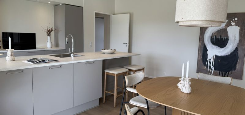Køkken-alrum i nybyggeri med rund spiseplads, køkkenø og rolige materialer