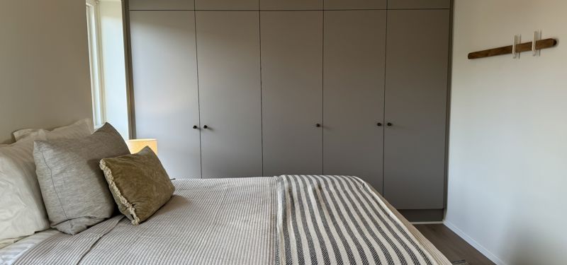 Soveværelse i nybyggeri med indbyggede skabe, rolige farver og bløde tekstiler