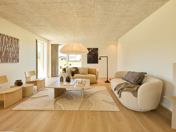 Stue fra eurodan-huse med lys sofa, rund loungestol, stort gulvtæppe, papirpendel, vægkunst og brede vinduer – inspiration til rolig boligindretning, nybyggeri og husdrømme.