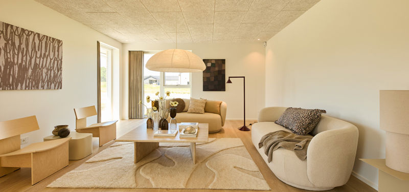 Stue fra eurodan-huse med lys sofa, rund loungestol, stort gulvtæppe, papirpendel, vægkunst og brede vinduer – inspiration til rolig boligindretning, nybyggeri og husdrømme.