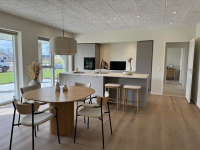 Åbent køkken-alrum i nybyggeri med spiseplads, køkkenø og moderne indretning