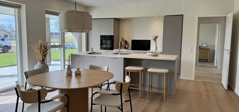Køkken-alrum fra eurodan-huse med moderne køkkenø, spiseplads, lyse materialer, store vinduer, åben rumfornemmelse og plads til både madlavning, gæster og familieliv – inspiration til nybyggeri, husbyggeri og et gennemtænkt nybygget hus.