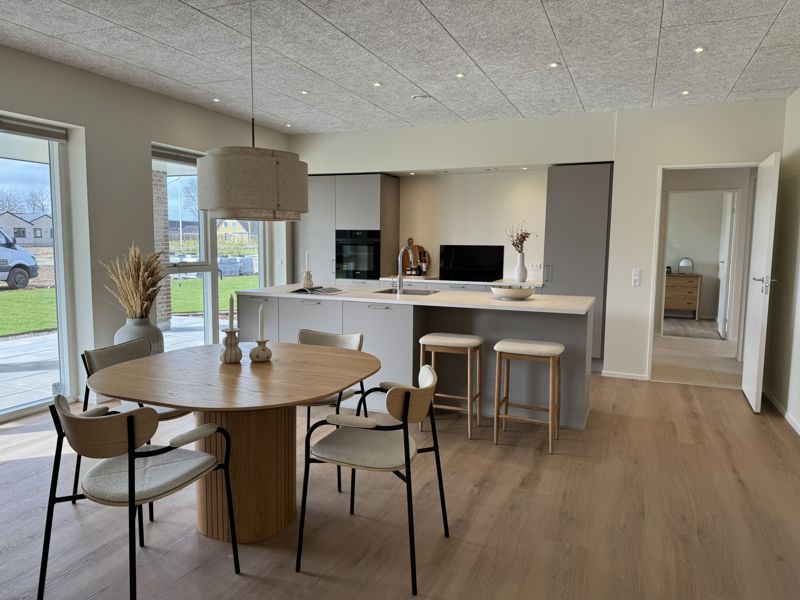 Køkken-alrum fra eurodan-huse med moderne køkkenø, spiseplads, lyse materialer, store vinduer, åben rumfornemmelse og plads til både madlavning, gæster og familieliv – inspiration til nybyggeri, husbyggeri og et gennemtænkt nybygget hus.
