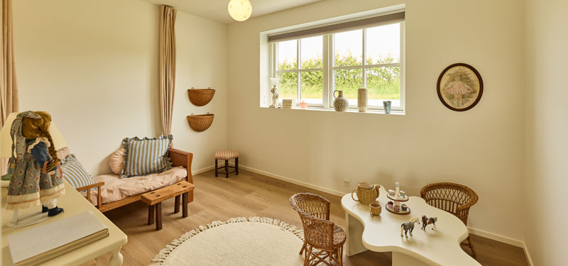 Børneværelse fra eurodan-huse med lille træseng, rundt tæppe, børnebord med kurvestole, legetøj, vægkurve og sprossevindue – inspiration til trygge børnerum i nybygget hus.