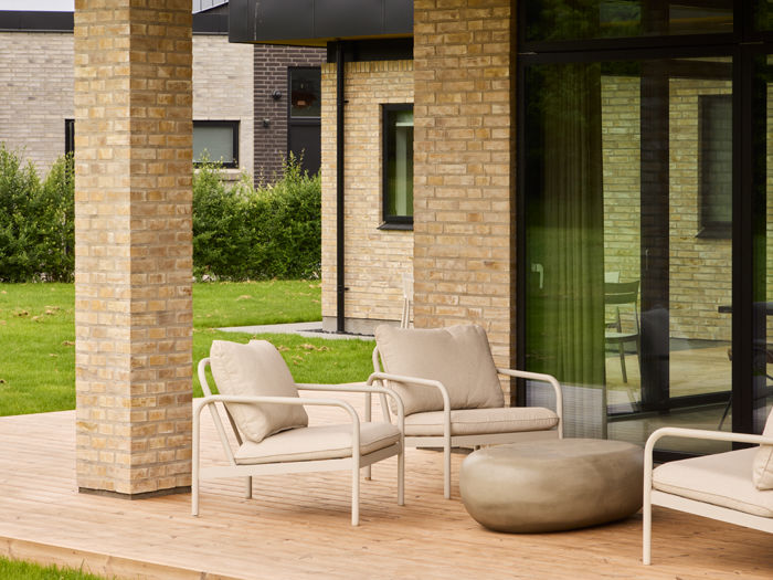 Overdækket terrasse fra eurodan-huse med lyse murstenssøjler, træterrasse, store sorte vinduespartier og loungemøbler – inspiration til nybyggeri med uderum, terrassemiljø og moderne husdrømme.