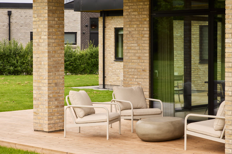 Overdækket terrasse fra eurodan-huse med lyse murstenssøjler, træterrasse, store sorte vinduespartier og loungemøbler – inspiration til nybyggeri med uderum, terrassemiljø og moderne husdrømme.