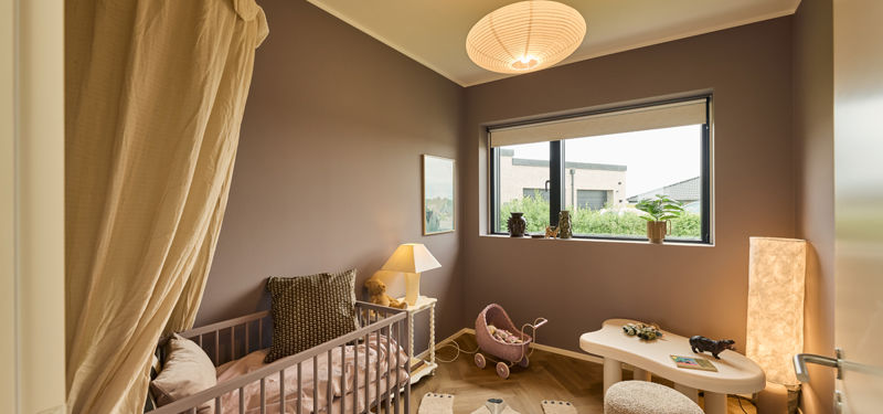 Børneværelse fra eurodan-huse med brun væg, tremmeseng, lille børnebord, dukkevogn, papirpendel og stort vindue – inspiration til hyggeligt børneværelse i nybygget hus.