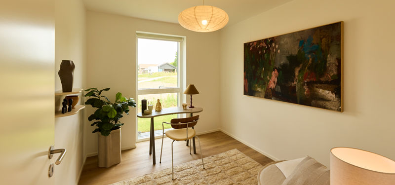 Kontor fra eurodan-huse med skrivebord ved vindue, loungestol, vægkunst, plante, gulvtæppe og rund pendellampe – inspiration til hjemmekontor i nybyggeri.