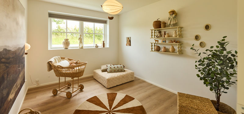 Børneværelse fra eurodan-huse med kurvevugge, lav daybed, rund gulvtæppe, væghylder med legetøj, grøn plante og stort sprossevindue – inspiration til familieliv i nybyggeri.
