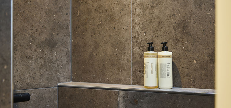 Indbygget shampoohylde i bruseniche med mørke fliser og plads til sæbe og plejeprodukter – inspiration til badeværelset i et nyt hus.