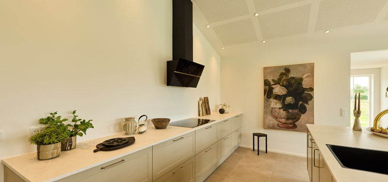 Køkken fra eurodan-huse med lange beige køkkenskabe, lys bordplade, sort emhætte, kogesektion, akustikloft og kunst på væggen – inspiration til køkkendesign i nybygget hus.